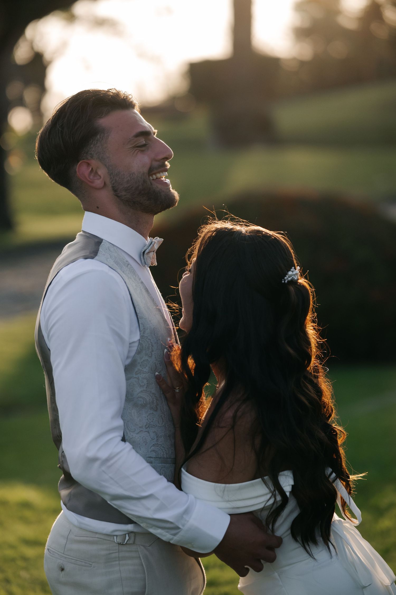 A couple shares a joyful moment together during golden hour in a park setting, with sunlight creating a warm backlit glow.