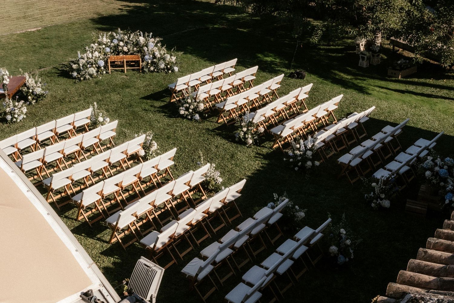 Aerial view of an outdoor wedding ceremony setup with wooden chairs and floral arrangements in a garden setting.