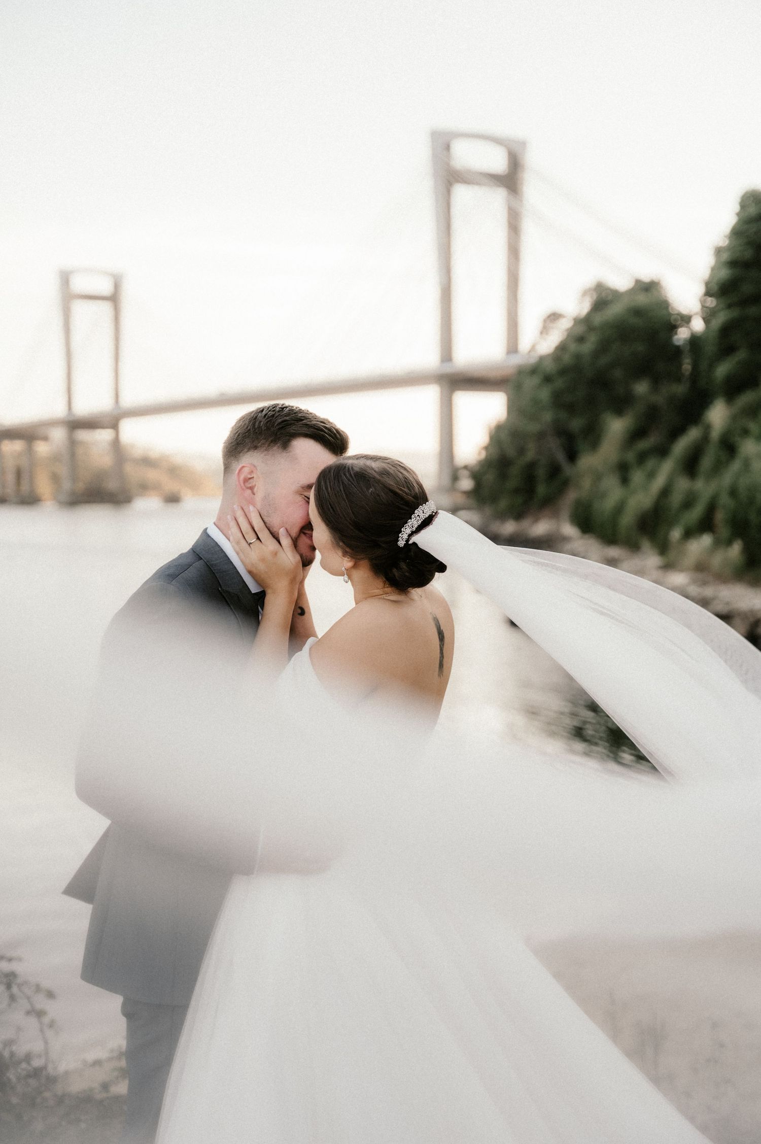 A couple in wedding attire share a romantic moment with the Golden Gate Bridge visible in the background.
