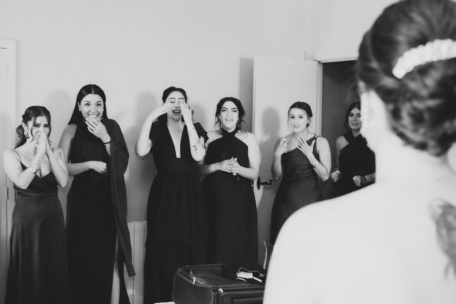 Wedding party members in black dresses and formal wear pose together against a white backdrop.