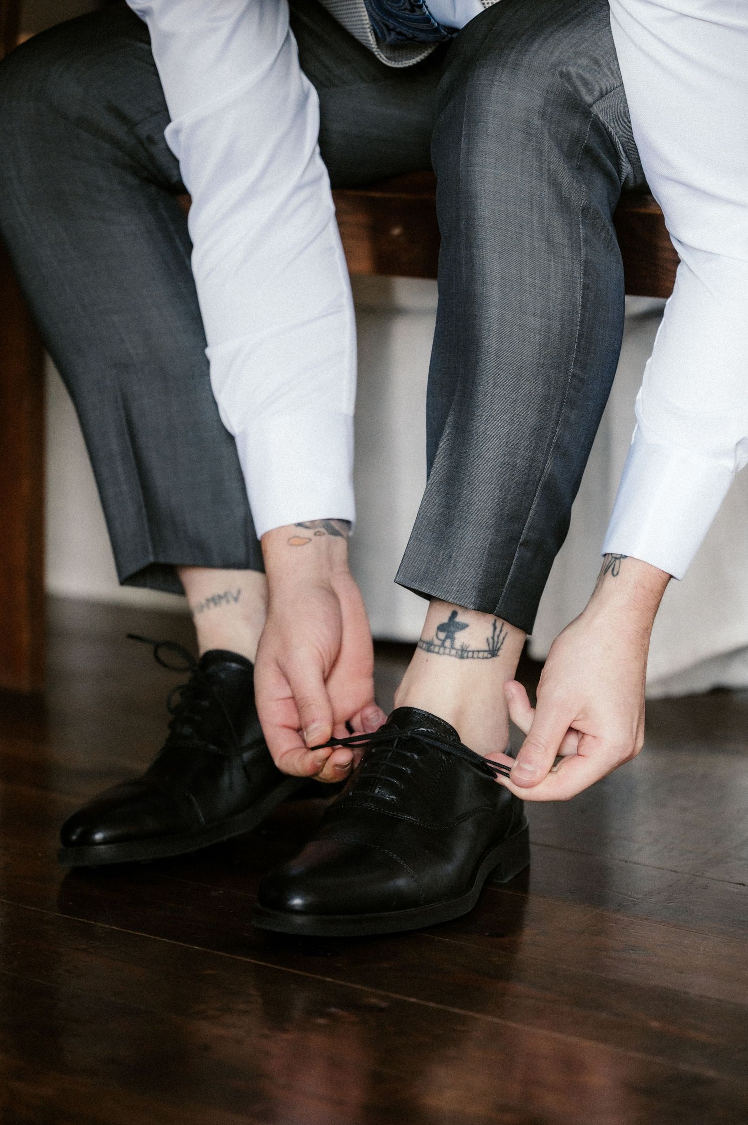 Close-up sequence of hands adjusting formal black dress shoes and socks on dark hardwood flooring.