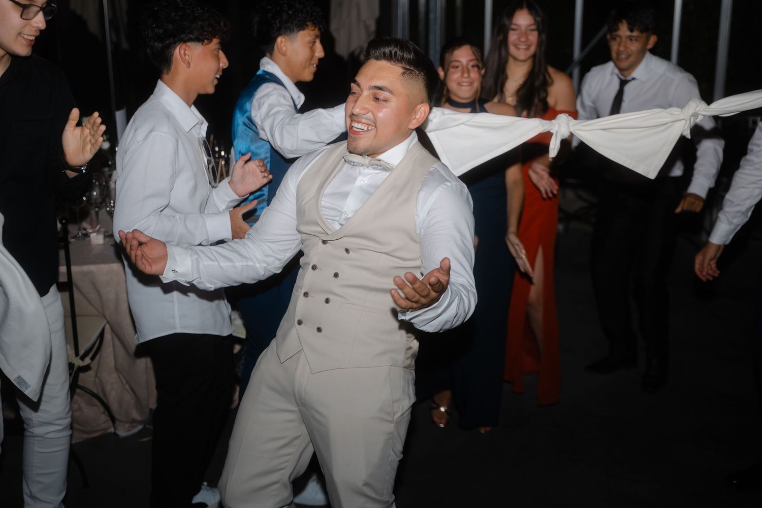 Wedding guests dance and celebrate during a lively reception party in a dimly lit venue.
