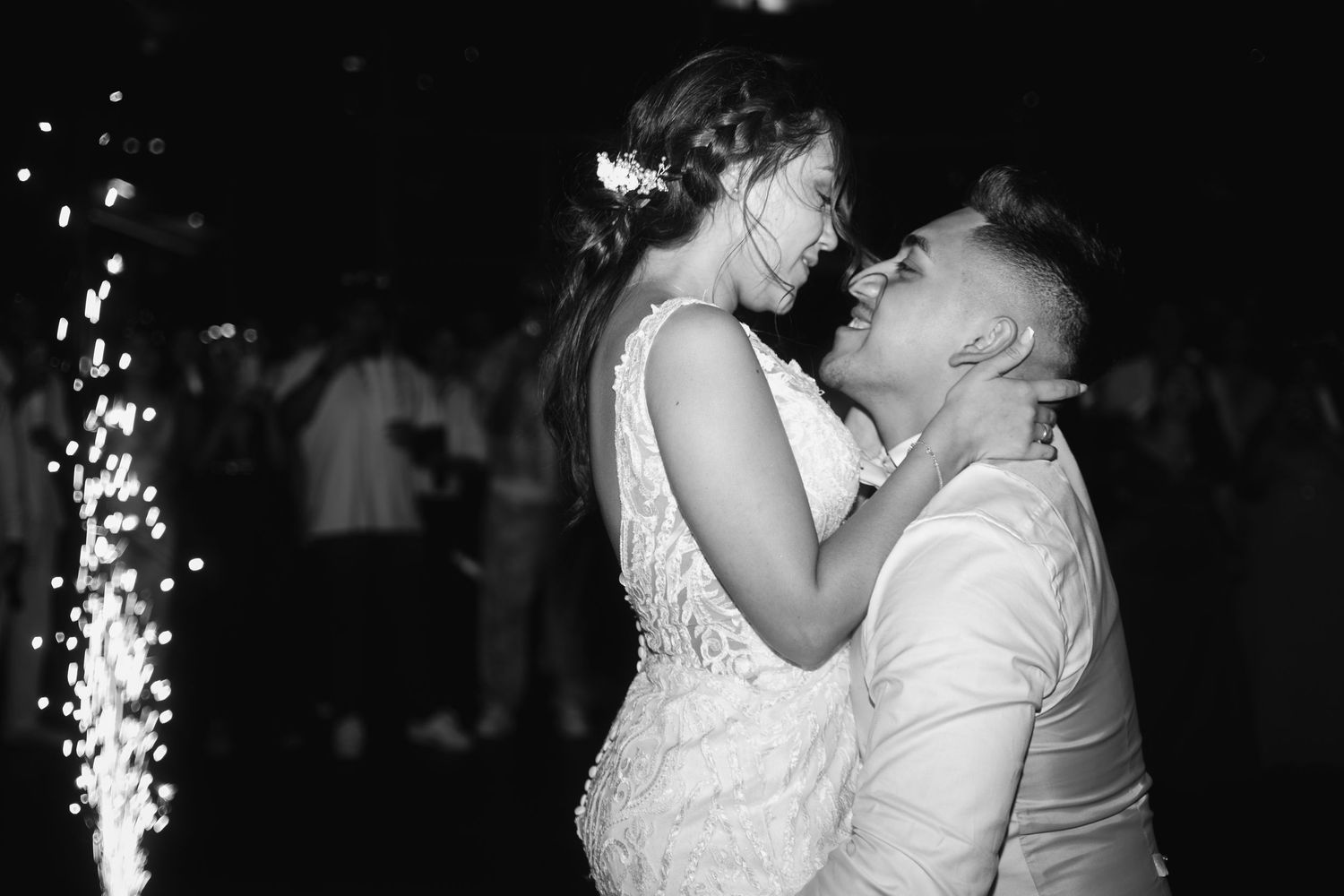 A couple shares a romantic kiss on their wedding day while sparklers create a magical glow in the background.