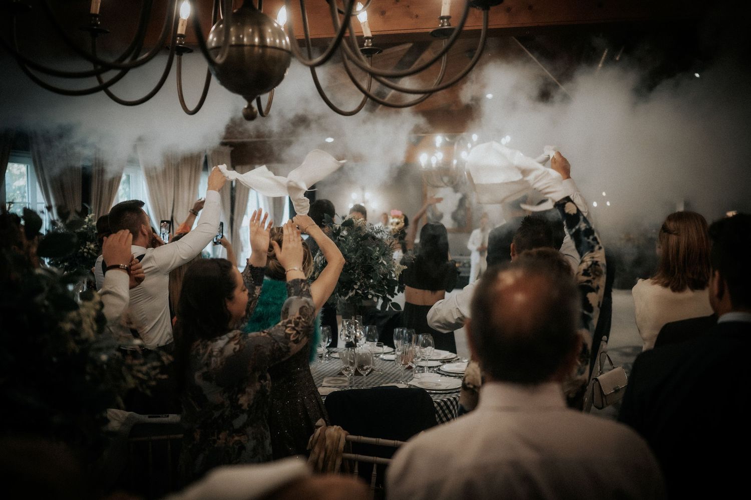 Wedding guests dance and celebrate on a dimly lit dance floor during an evening reception celebration.