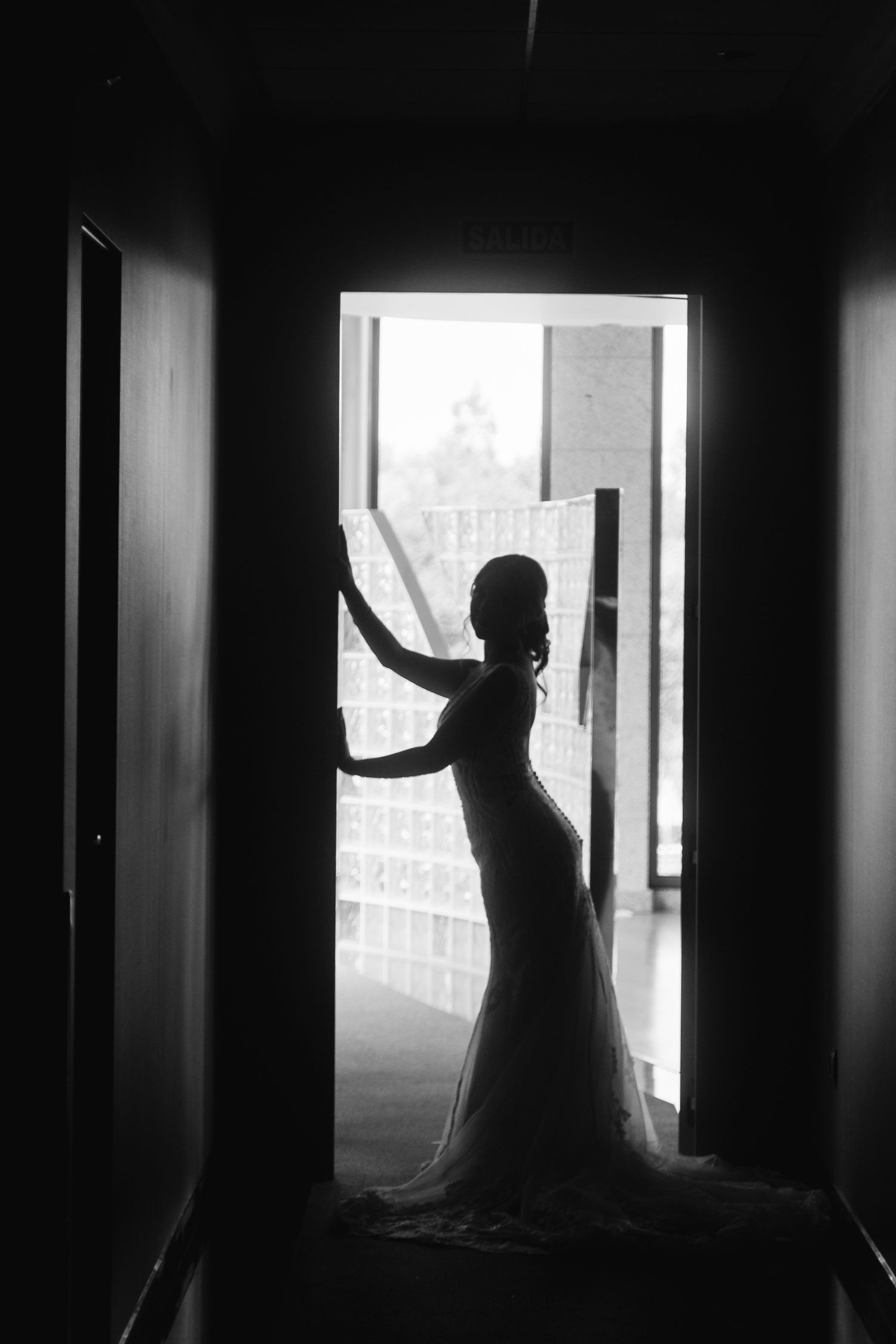Dramatic silhouettes of a bride in a dark hallway with bright windows creating a moody atmosphere.