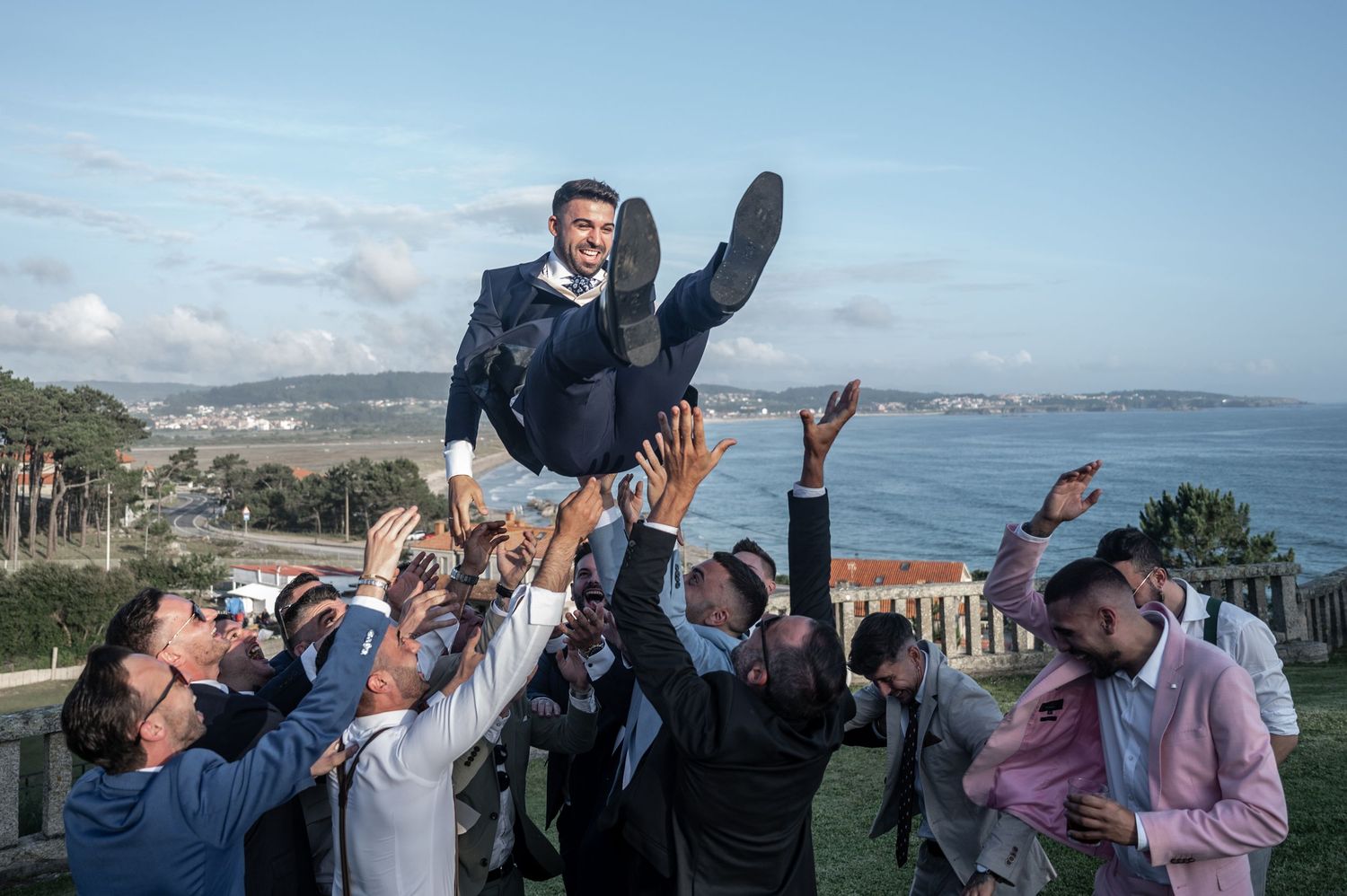 Wedding party celebrating outdoors with scenic coastal views and blue skies in the background.