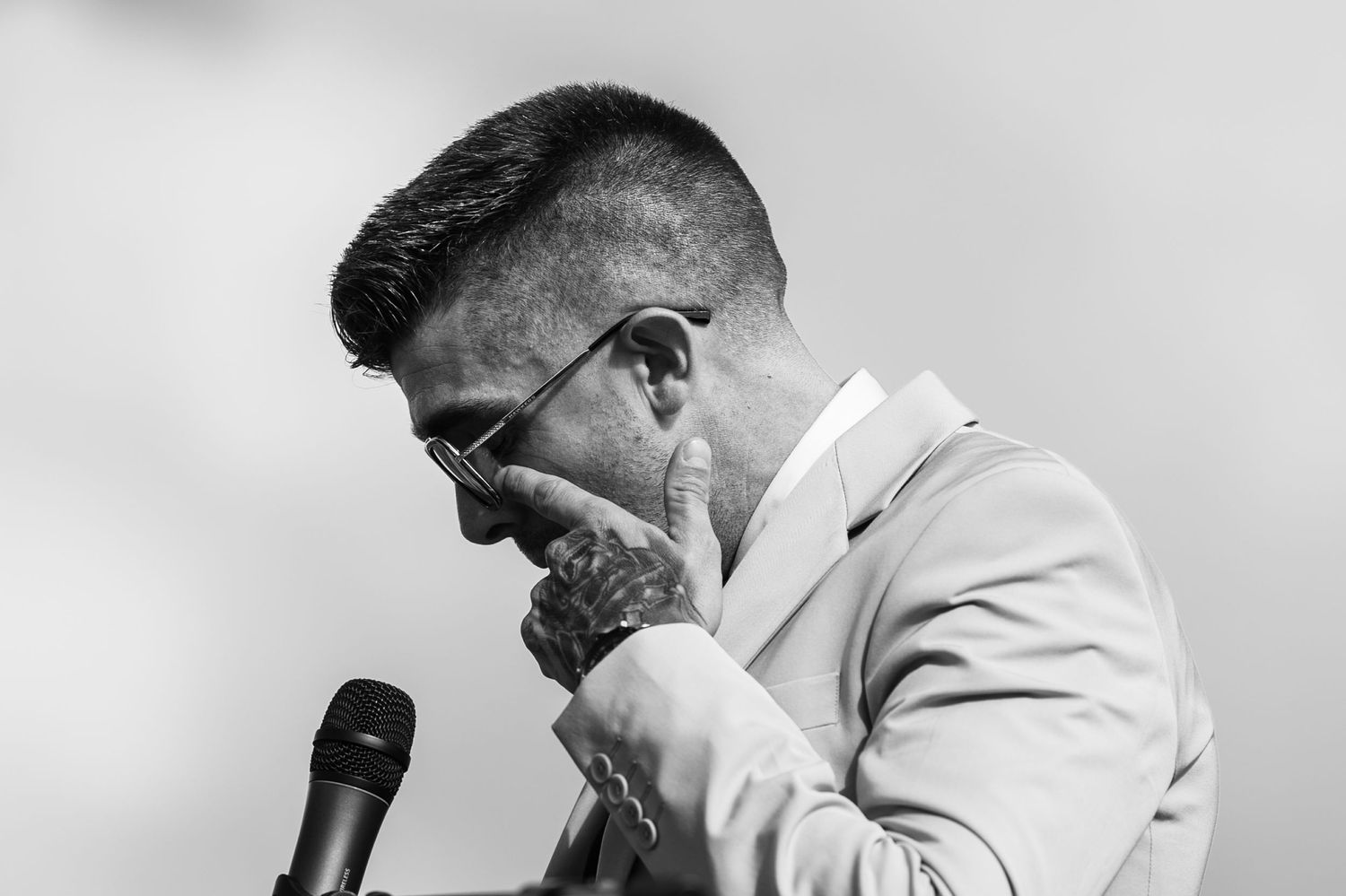 A person in a white suit and dark glasses performs on stage with dramatic lighting and shadows.