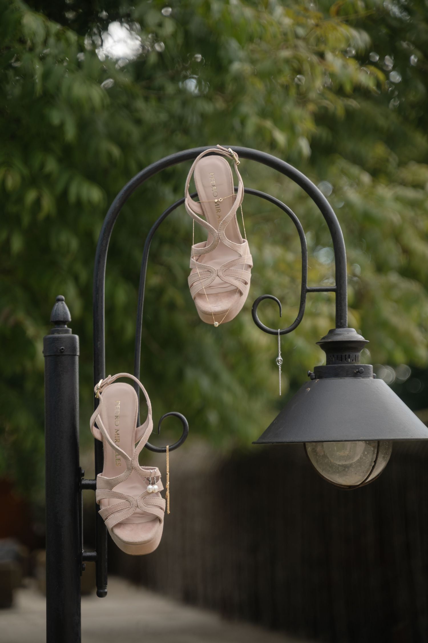 A beige face mask blows in the wind while hanging from a black outdoor lamp post against a blurred green background.