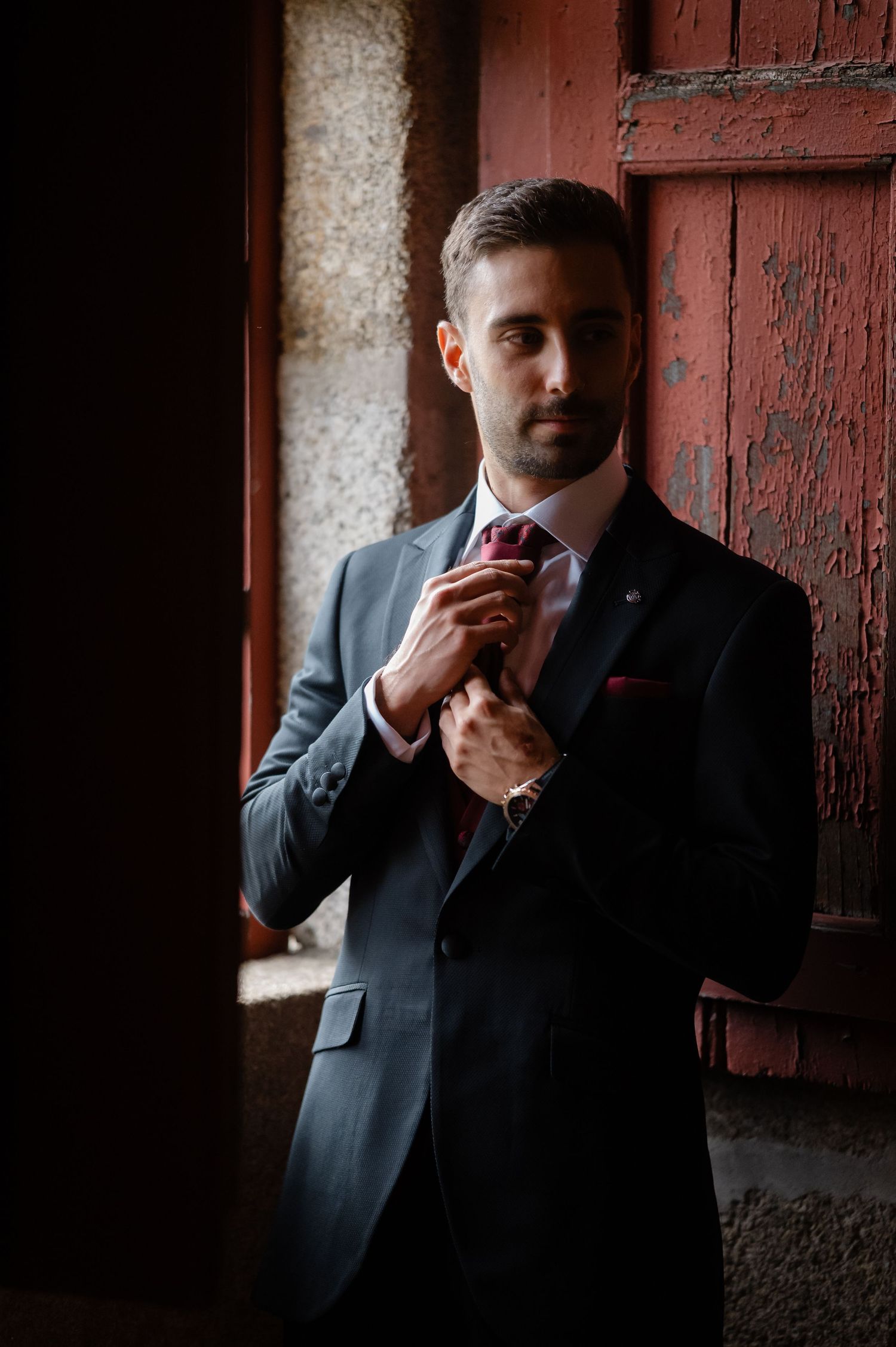 Multiple shots of someone in formal attire adjusting their tie against a rustic brick background.