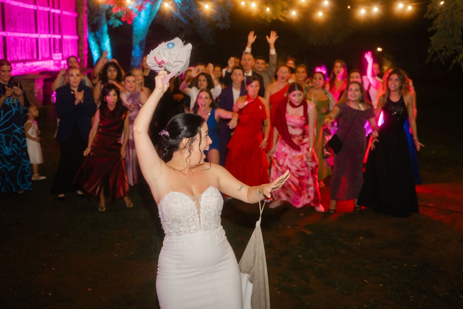 Wedding party dancing and celebrating on a dance floor illuminated by string lights and pink uplighting.