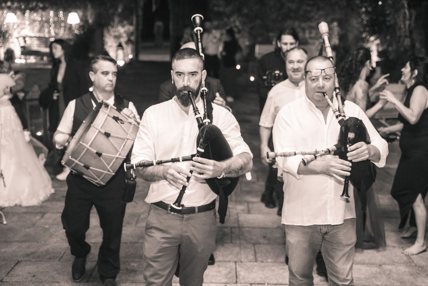 Three musicians perform at an outdoor event with bagpipes and drums in a vintage black and white photograph.