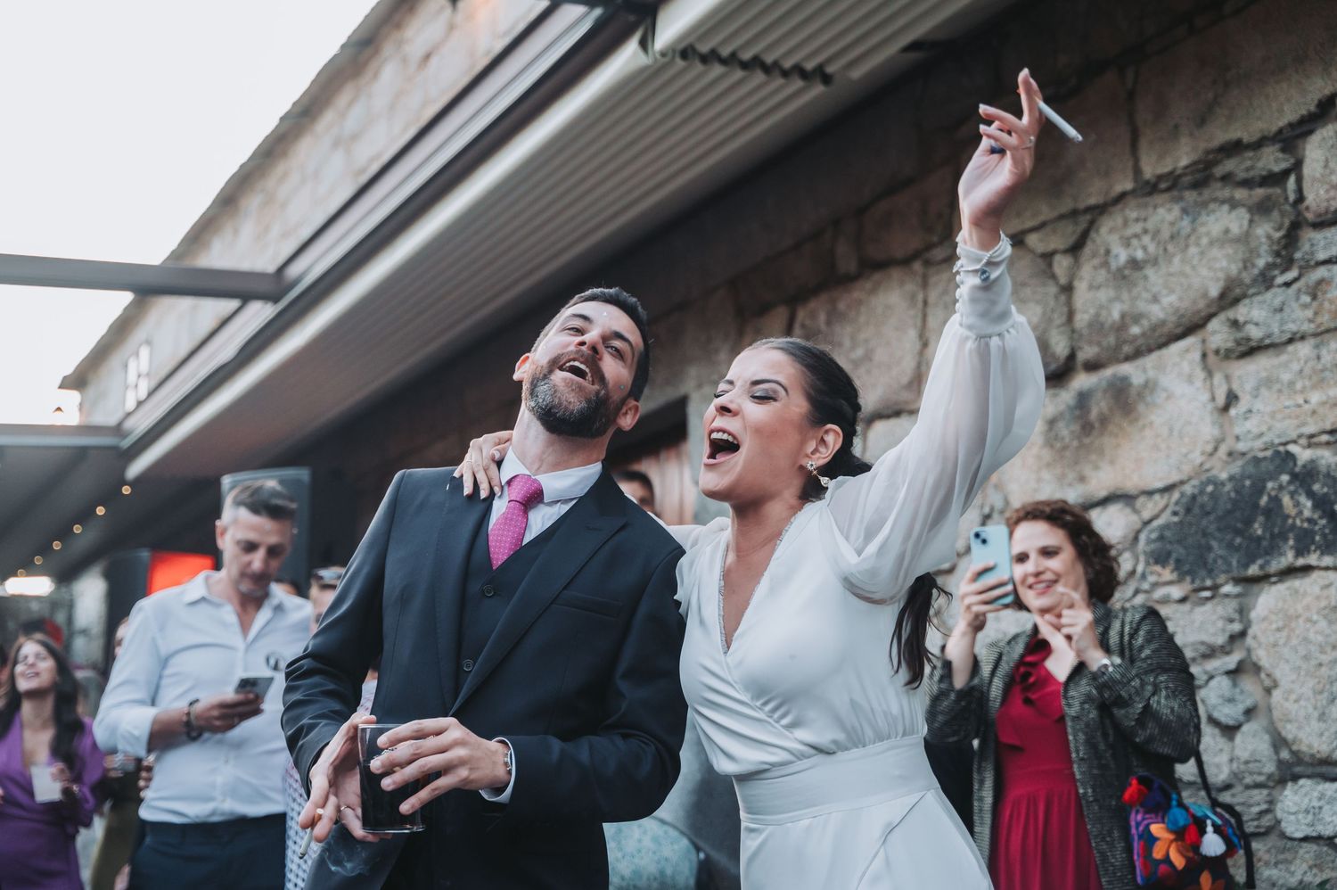 Wedding guests laugh and dance together during a joyous celebration at a rustic stone venue.