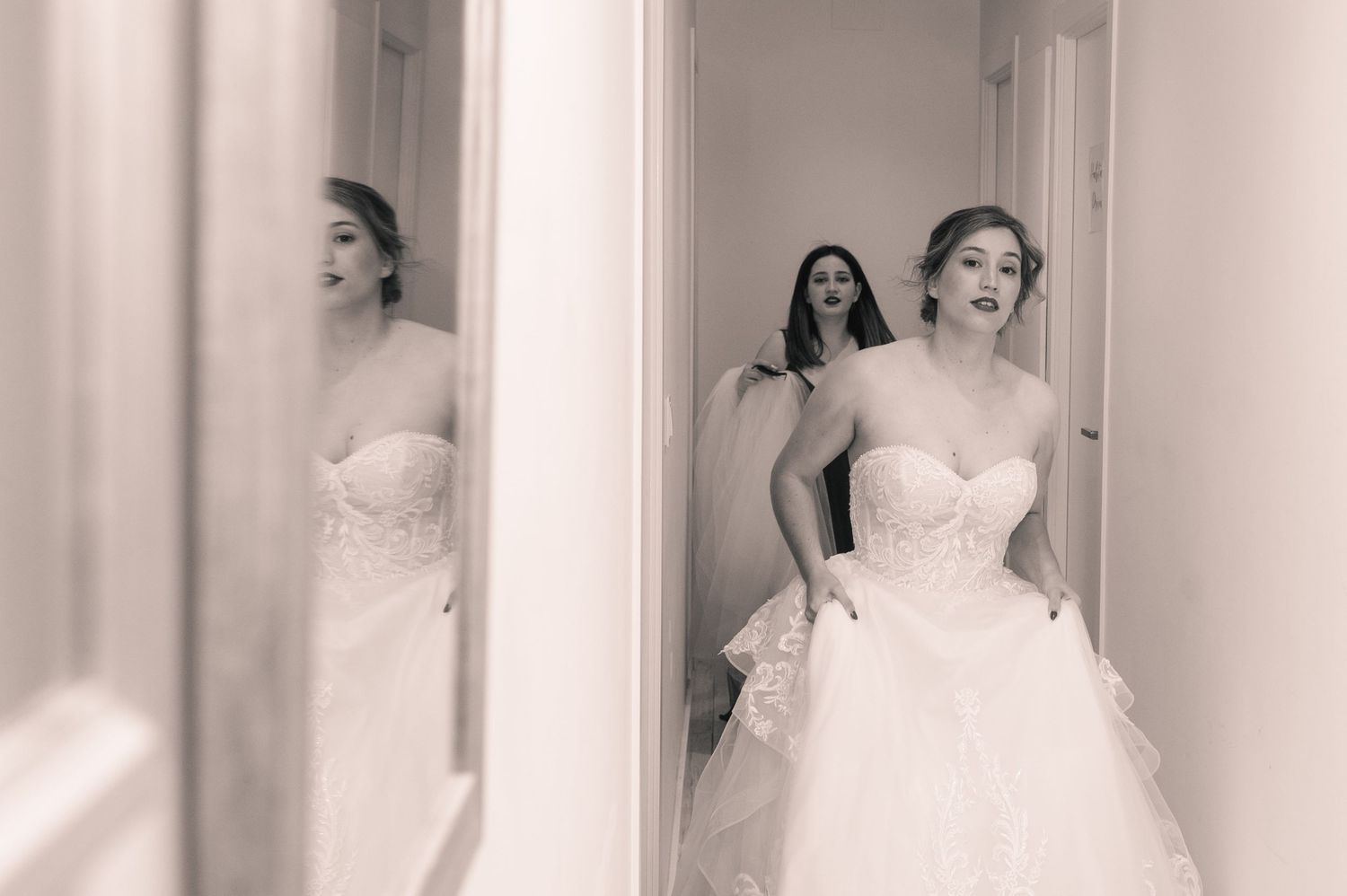 A bride in a white strapless wedding gown stands in a doorway with natural light illuminating her silhouette.
