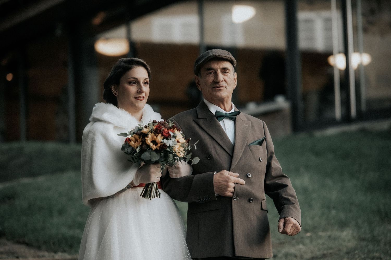 A couple in winter wedding attire embraces outdoors in a moody, romantic setting.