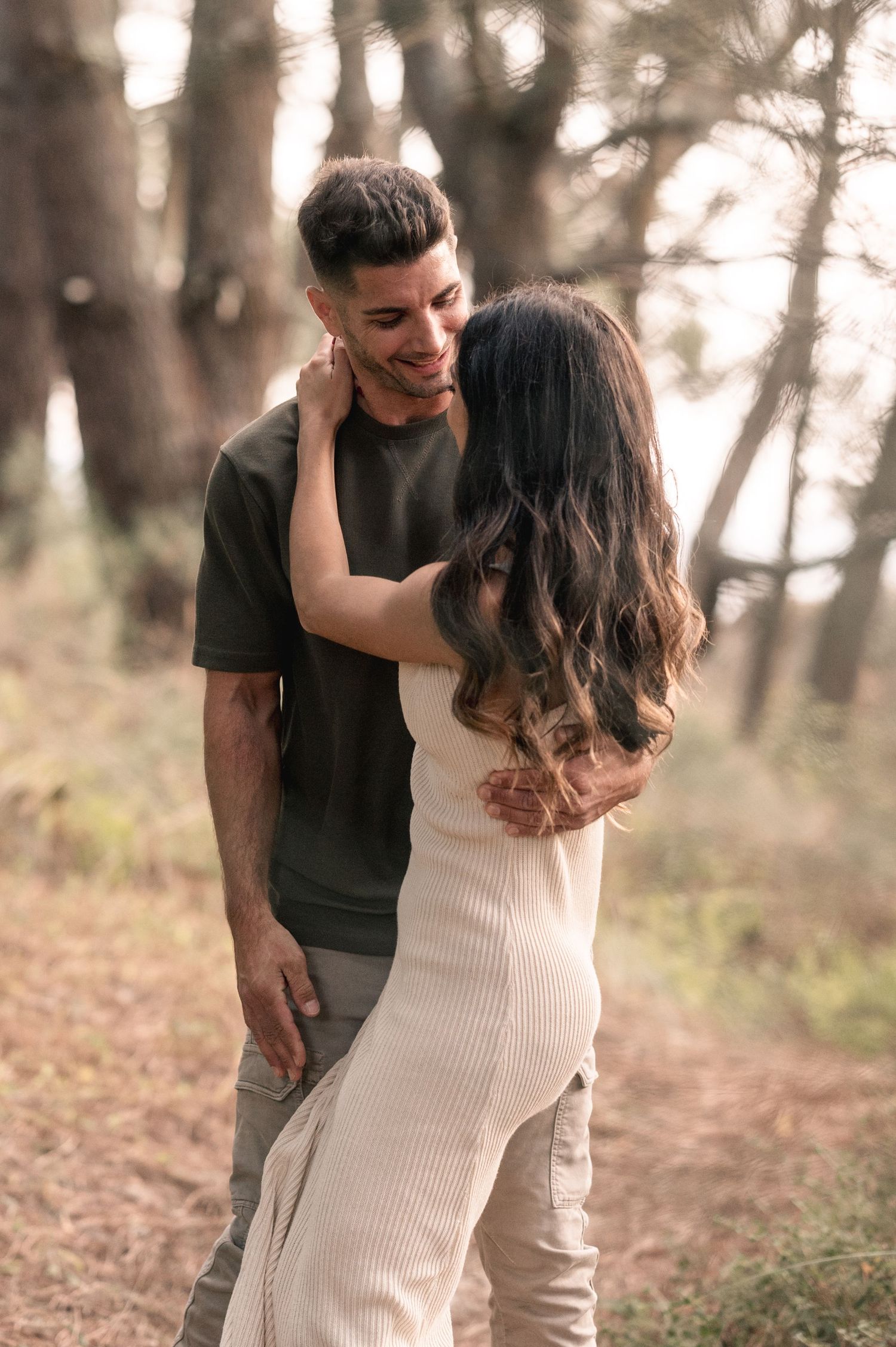 A loving couple shares an intimate moment while standing together on a wooded trail.