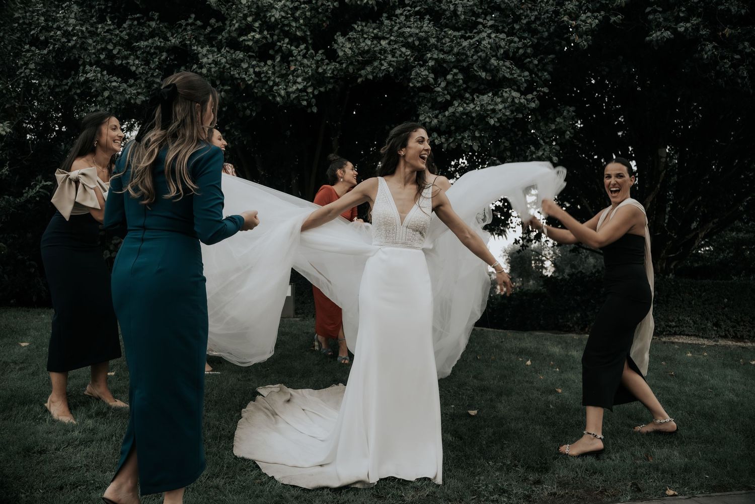 Wedding party members walk together across a dark grassy lawn with flowing white dress in motion.