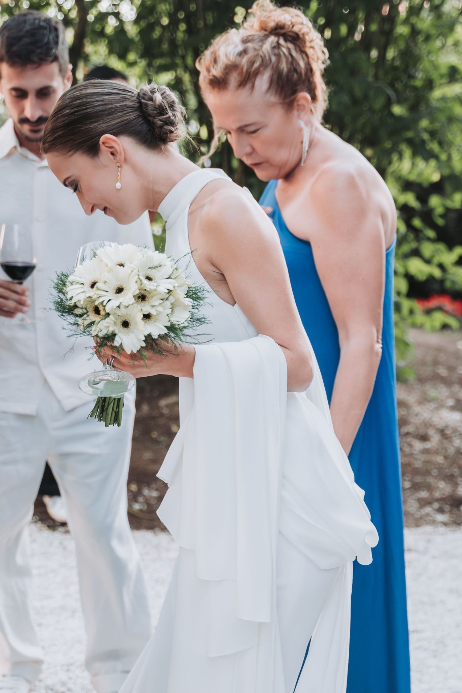 Bridesmaids in blue dresses and white gowns hold elegant white floral bouquets during an outdoor ceremony.
