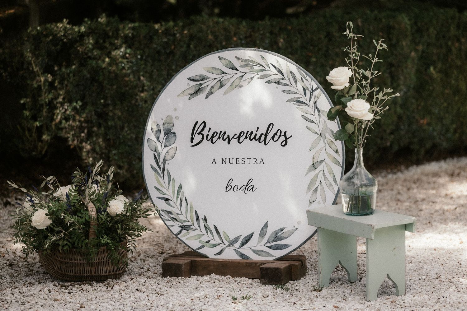 A round welcome sign with 'Bienvenidos' text and floral design sits next to decorative glass bottles and greenery.