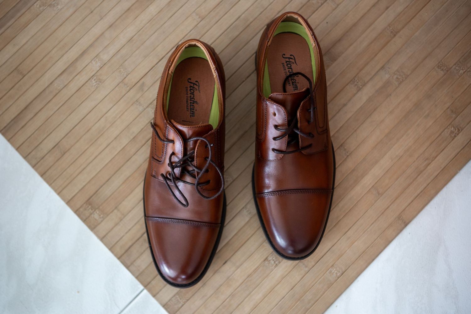 Brown leather dress shoes arranged in a diagonal line on light wooden flooring.