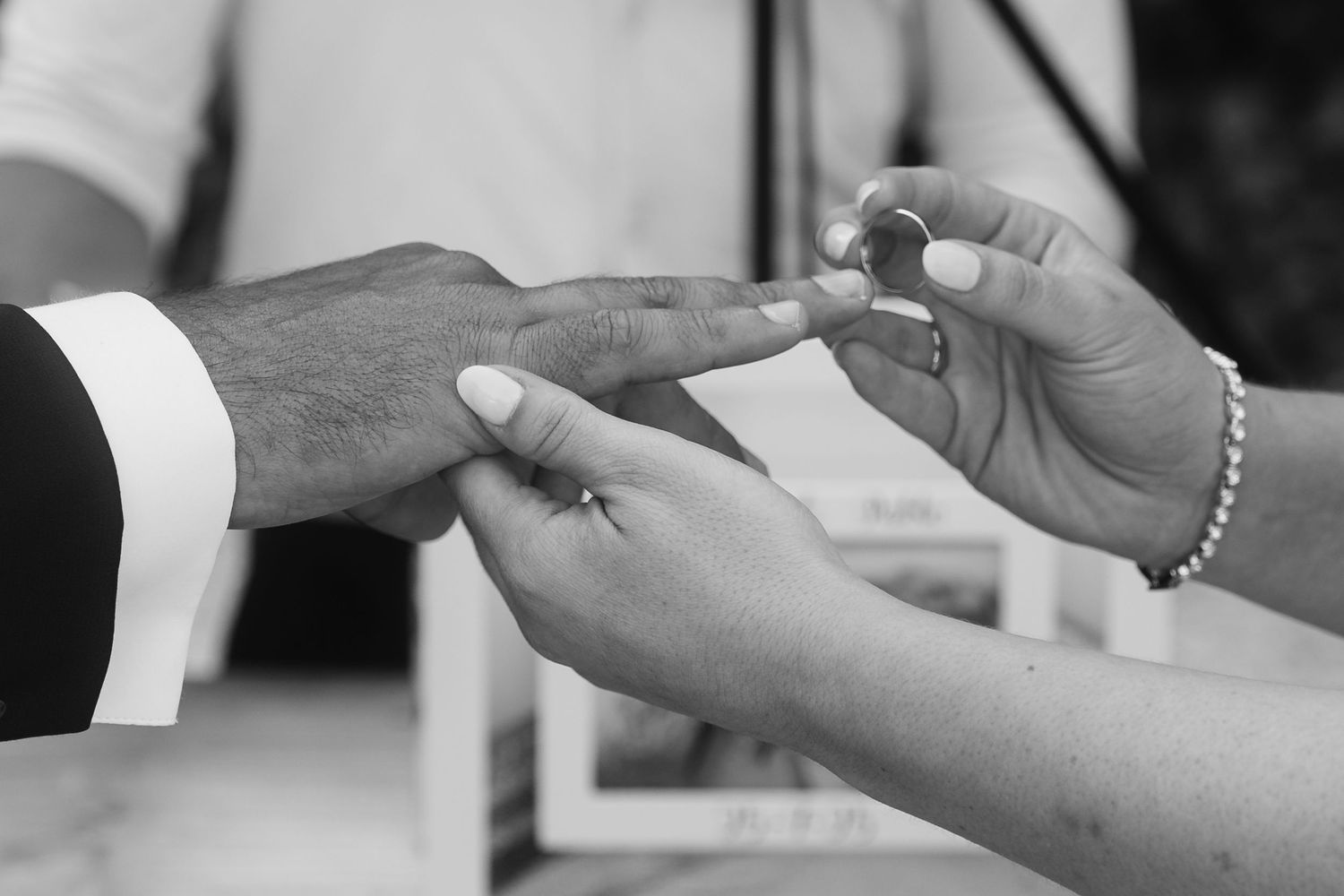 Close-up of hands exchanging wedding rings during an outdoor ceremony.