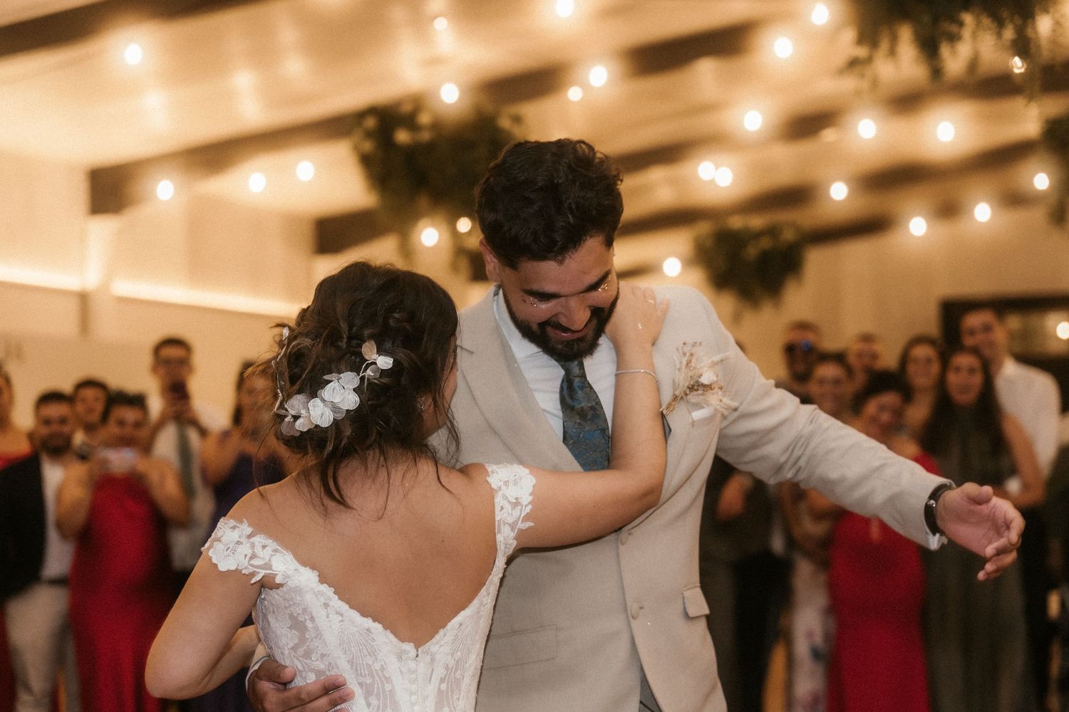 A couple shares their first dance at a wedding reception under warm lighting and decorative greenery.