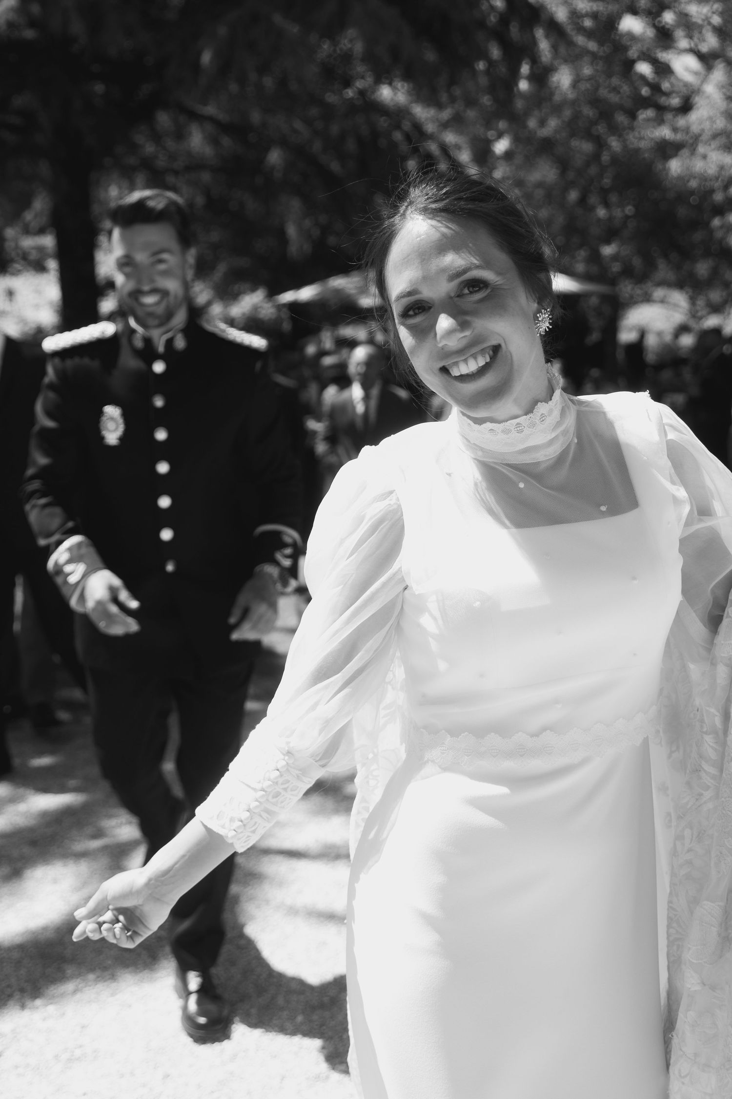 A joyful black and white wedding photo showing a bride in a white dress and a groom in military uniform outdoors.
