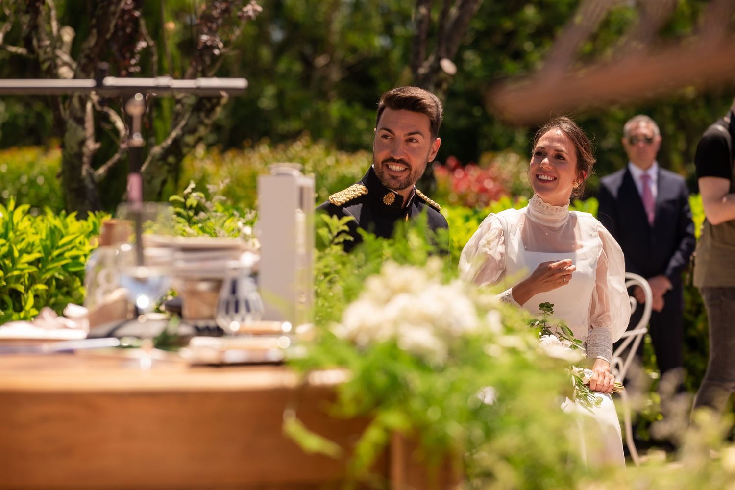 Guests celebrate at an elegant outdoor wedding reception with floral decorations and natural greenery.