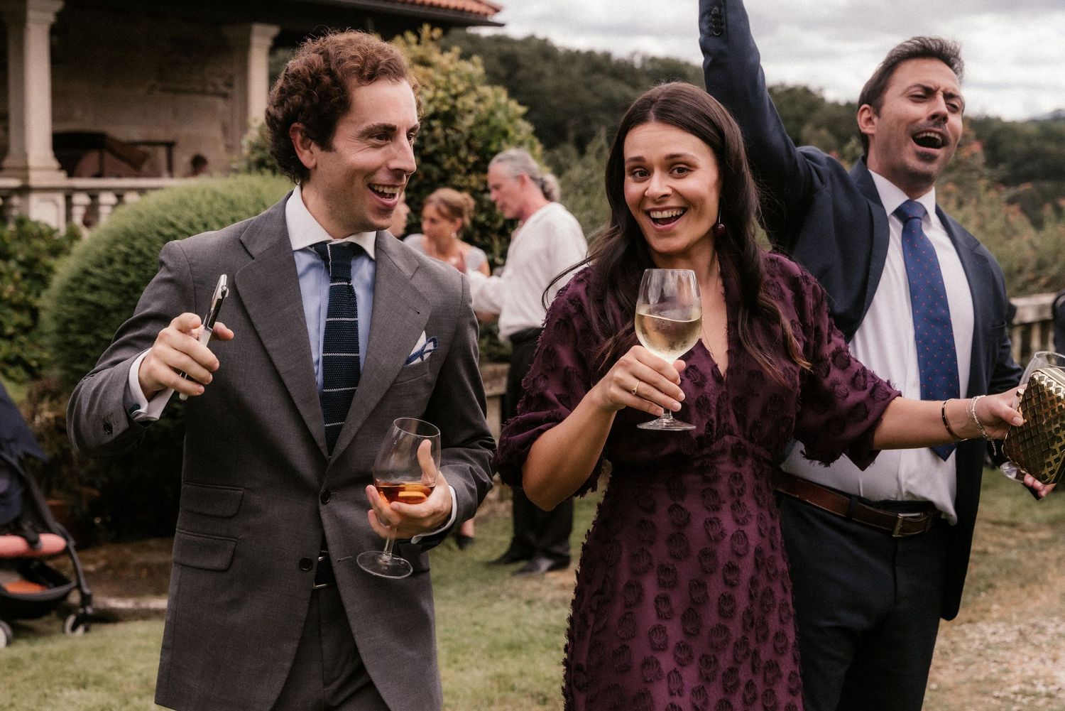 Wedding guests enjoying drinks and laughter at an outdoor celebration.