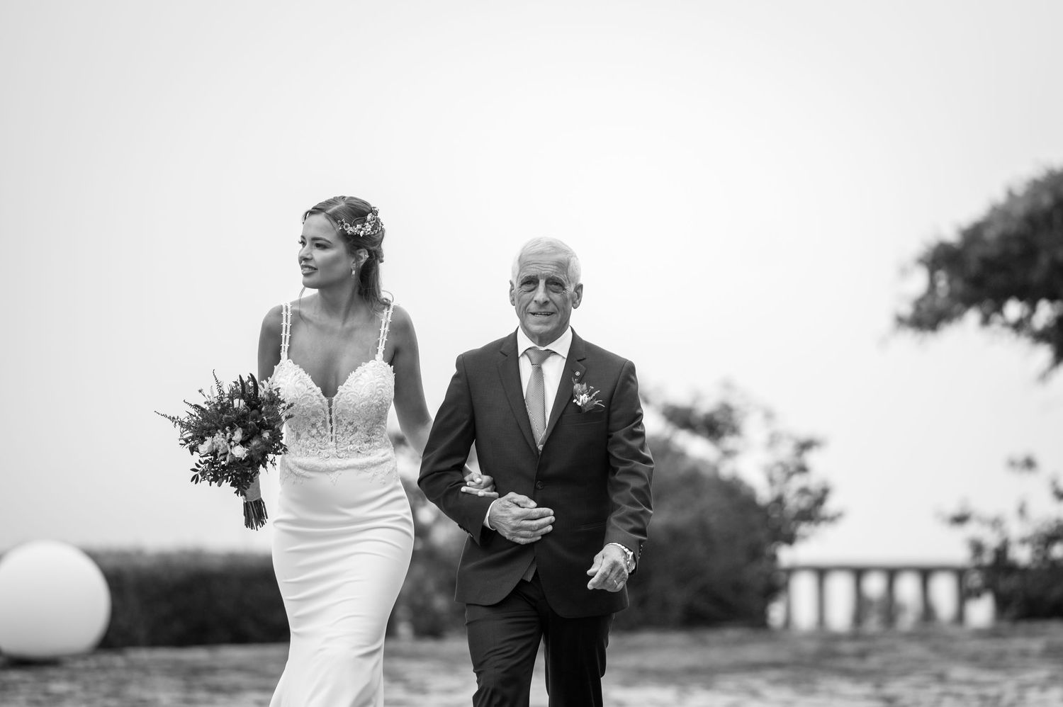 A bride and groom walk together holding champagne glasses during an elegant outdoor wedding celebration.