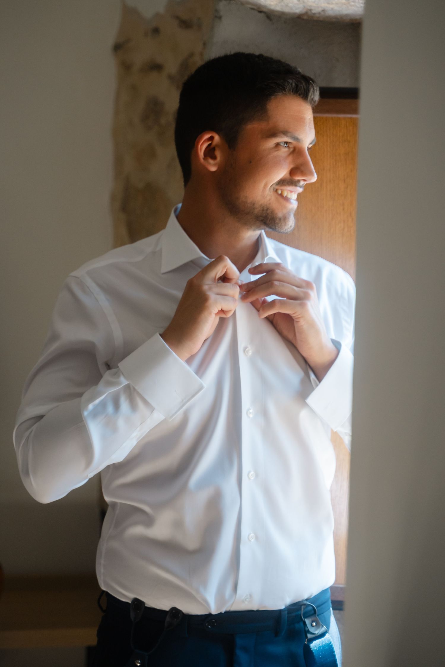 Man in white dress shirt adjusting collar while looking to the side in natural light.