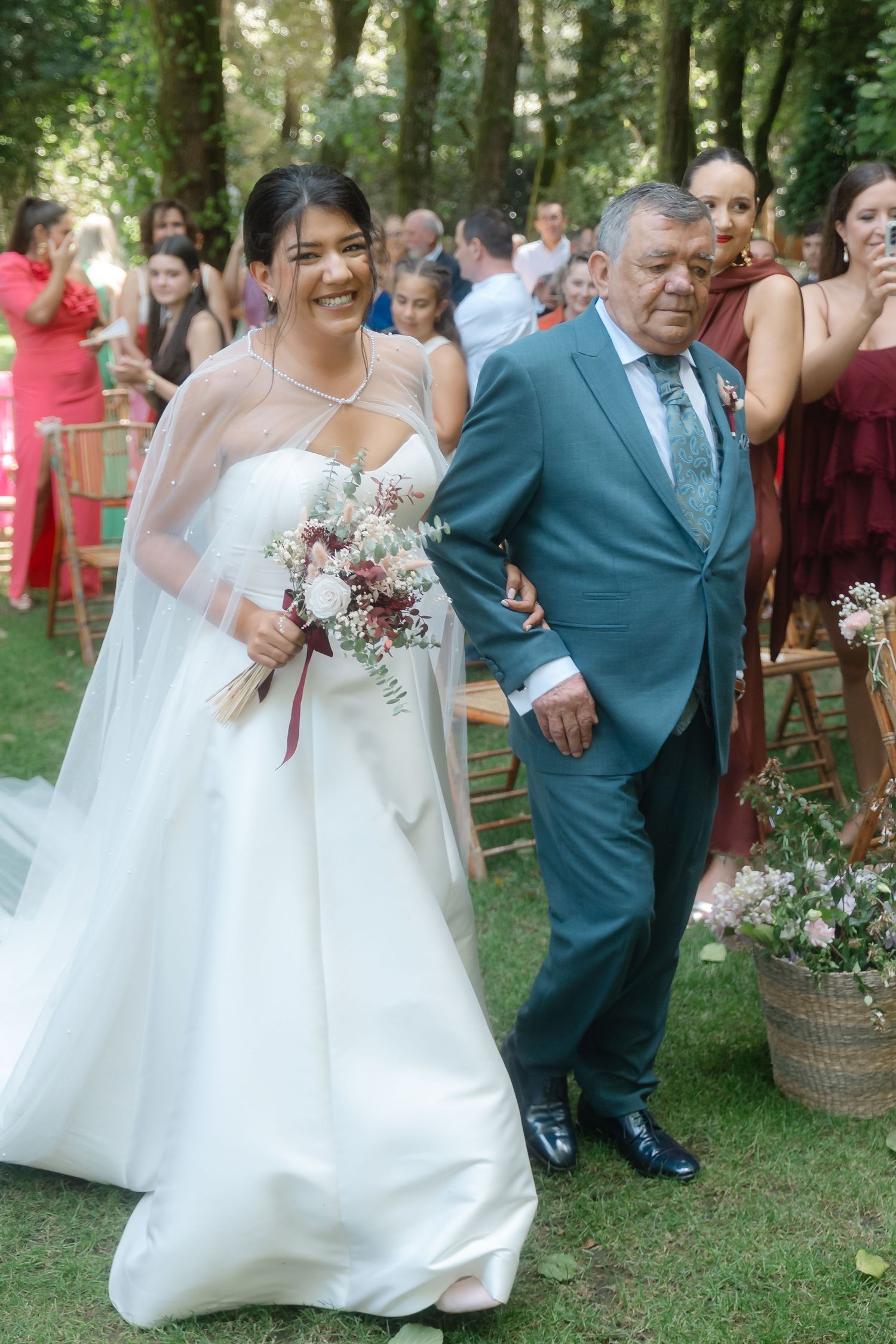 Newlyweds walking together through garden setting with wedding party and guests in background.