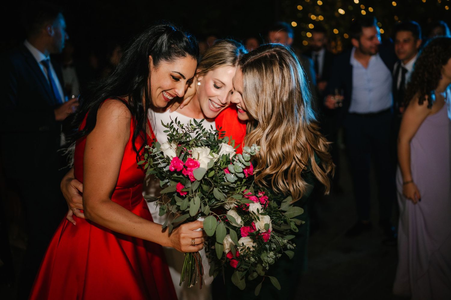Bridesmaids in colorful dresses gather for a joyful group photo with bouquets.