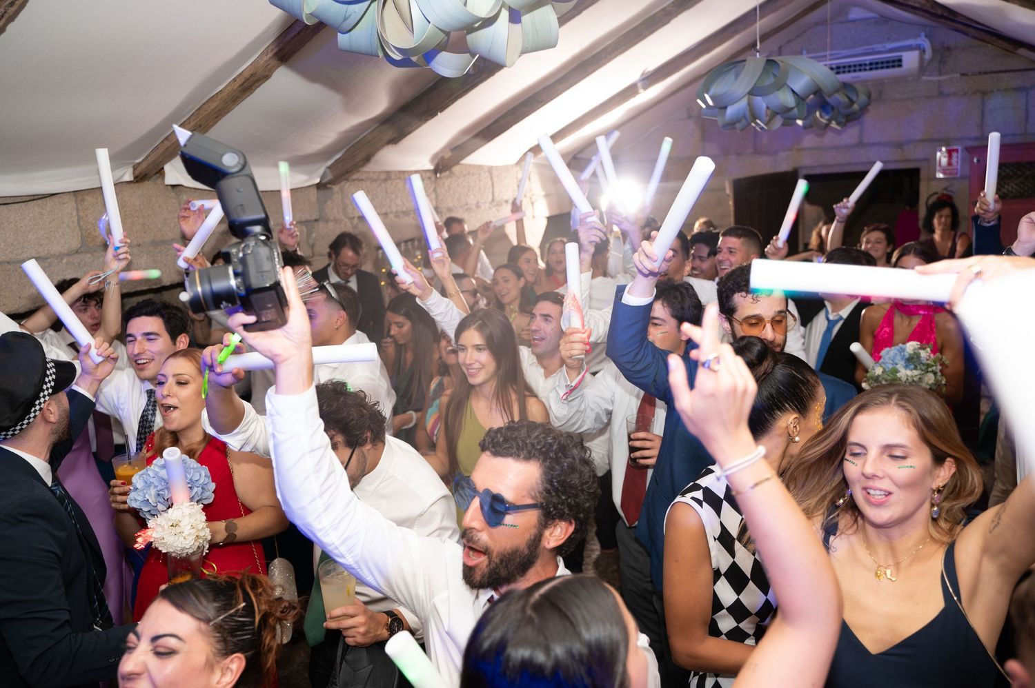 A crowd of people dancing and celebrating with their arms raised at a lively indoor party event.