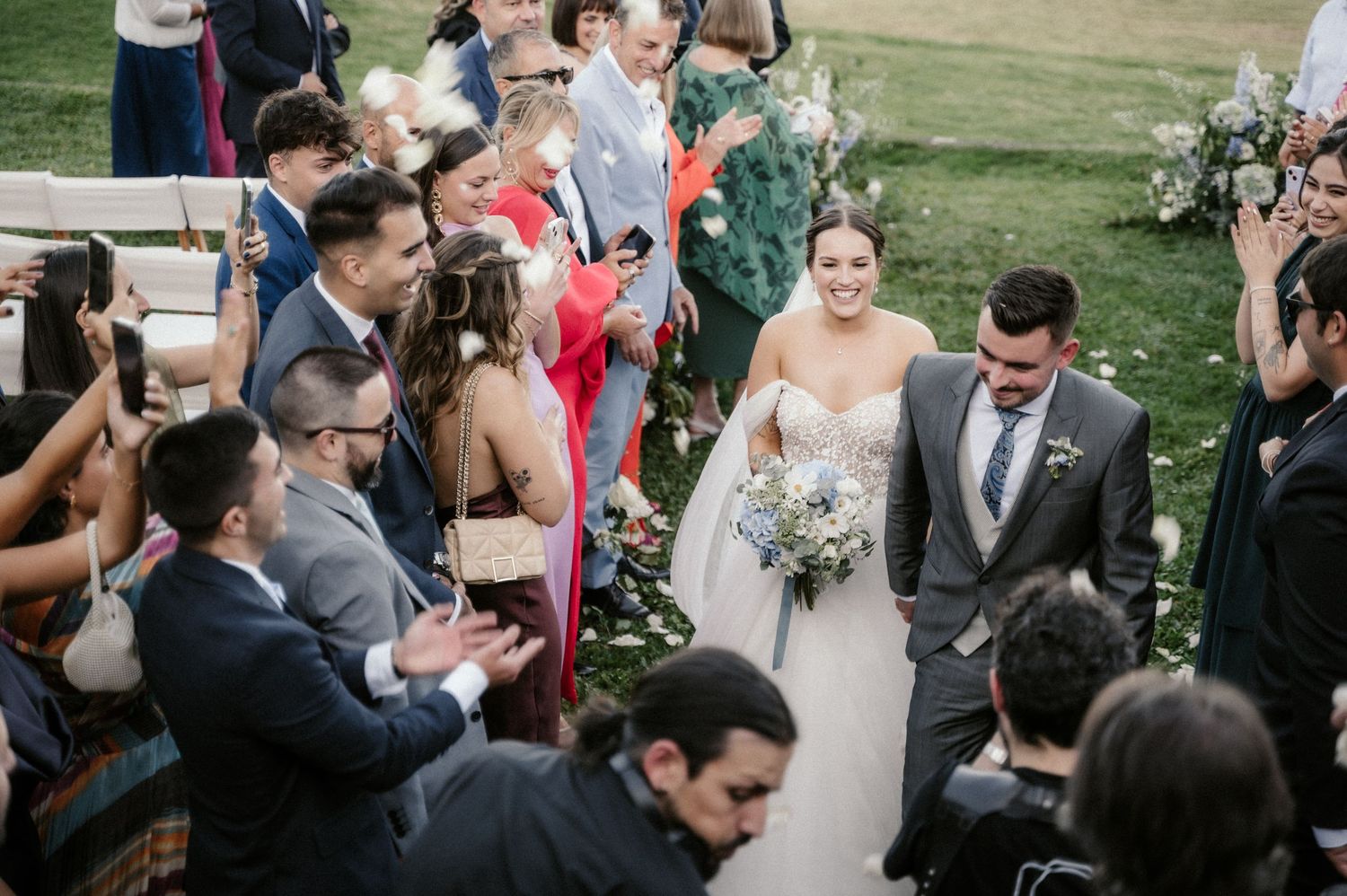 Wedding guests celebrate and take photos as newlyweds walk down the aisle after ceremony.