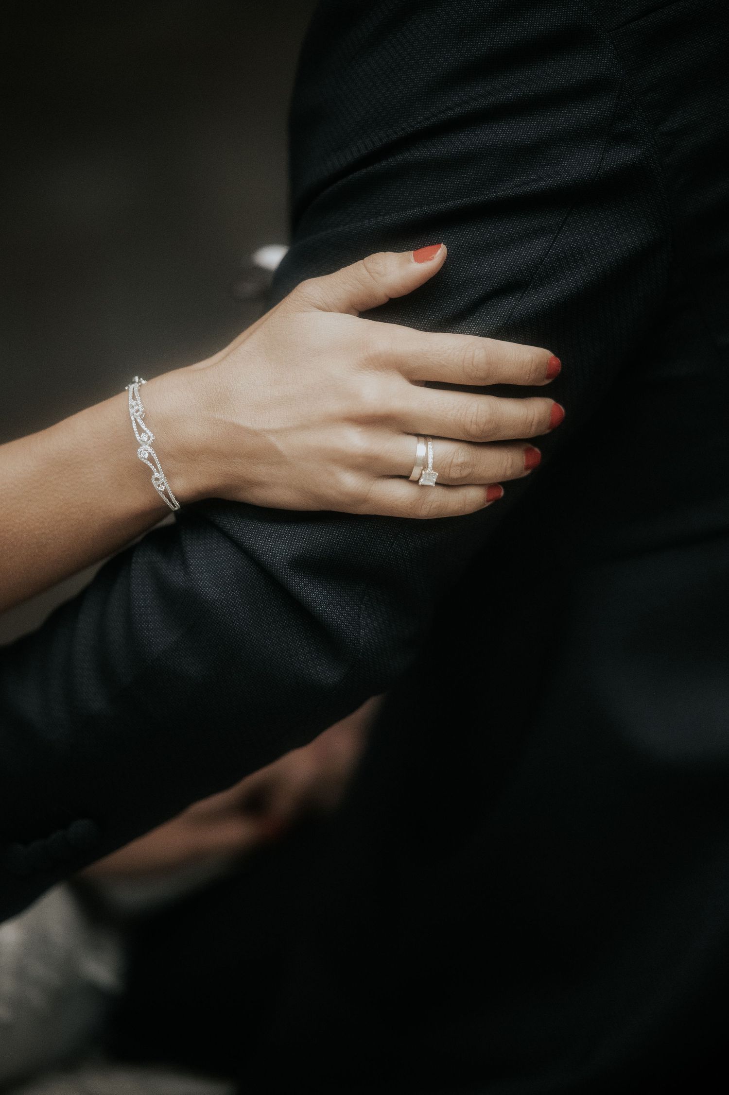 A close-up of a bride's hand with wedding ring and bracelet resting on dark fabric.
