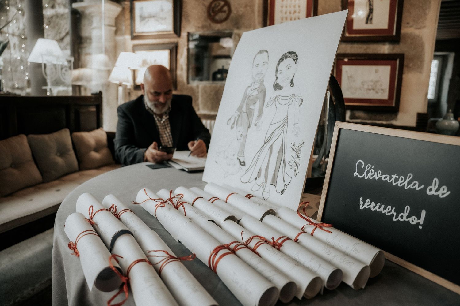 Artist works at a table with sketch displayed and rolled papers at a vintage cafe interior.