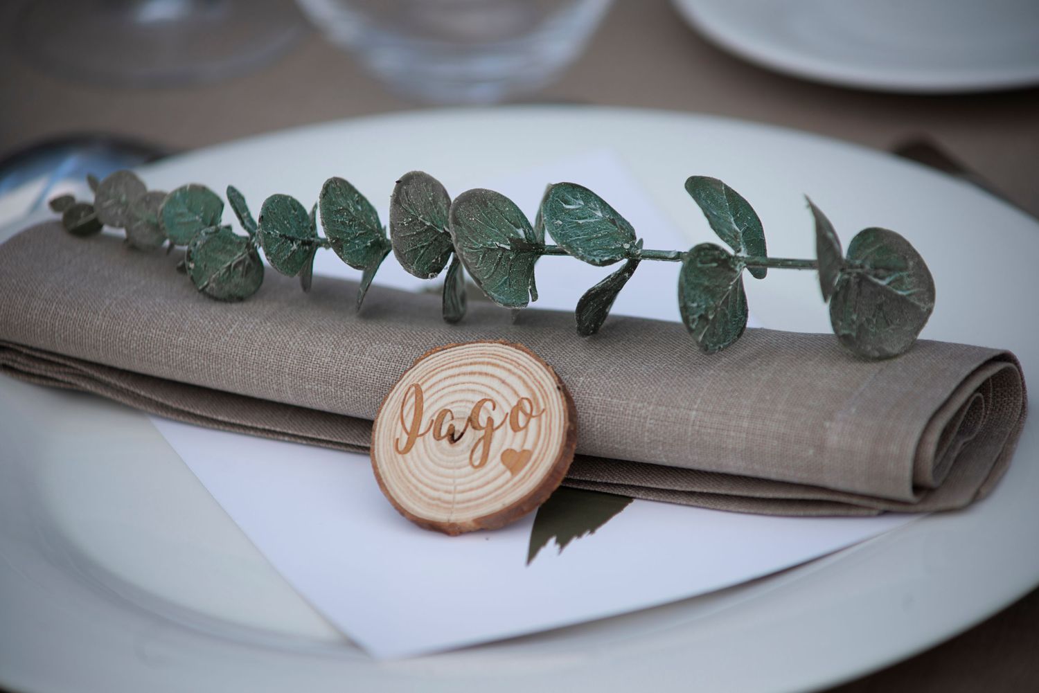 A rustic table setting with eucalyptus branches, white plates, and gray linen napkins arranged for dining.