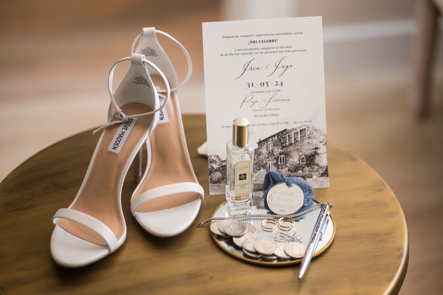 Elegant white bridal heels and wedding invitation displayed on wooden table with decorative accessories.
