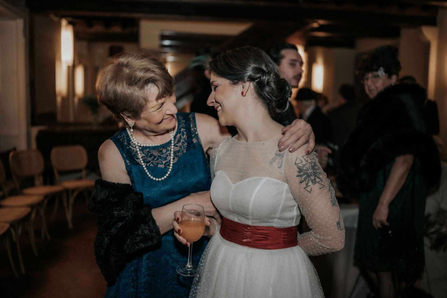 Wedding guests dance and celebrate together during an evening reception in a dimly lit venue.
