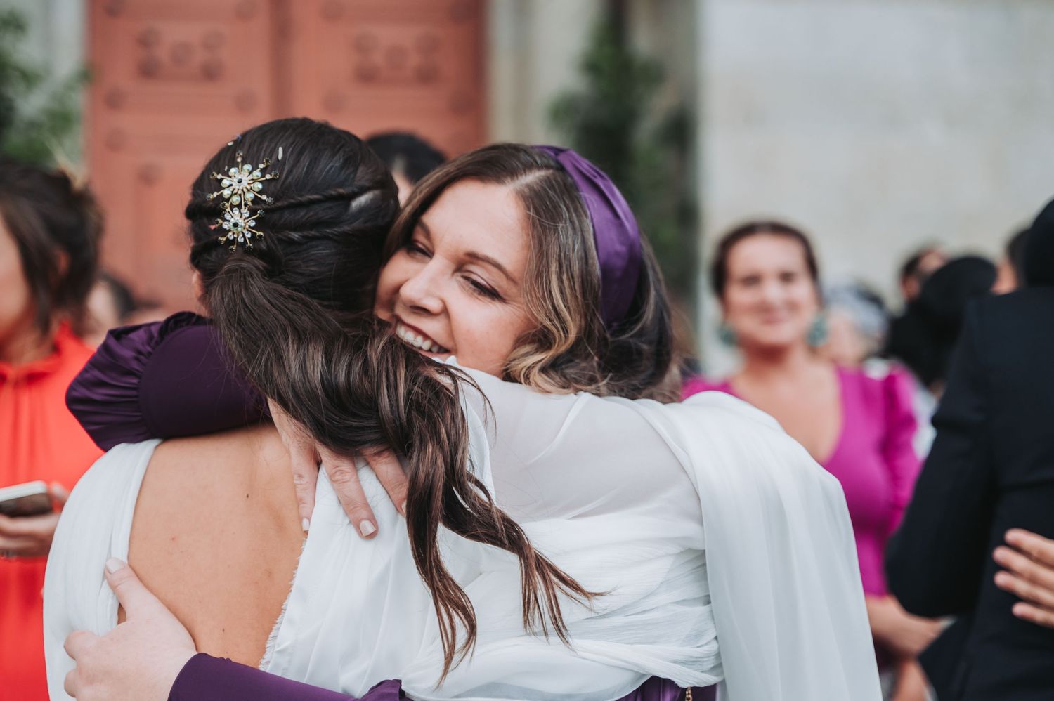 Two wedding guests share an emotional embrace at an outdoor celebration.