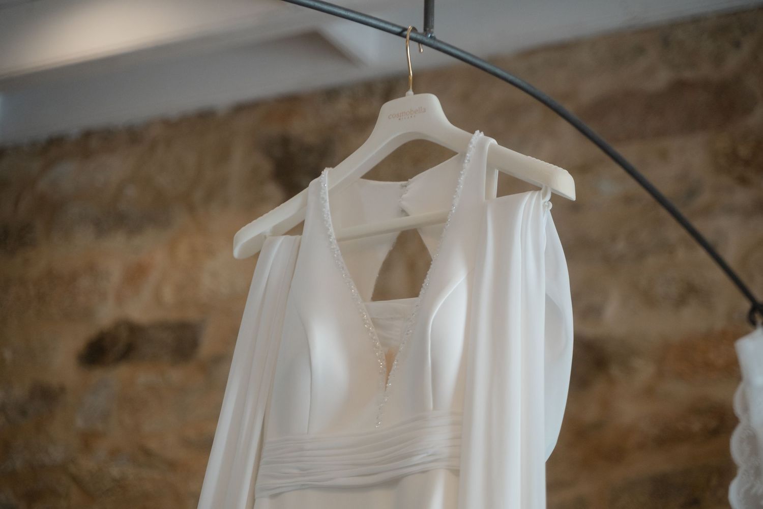 Multiple white wedding dresses displayed on hangers against a stone wall backdrop.