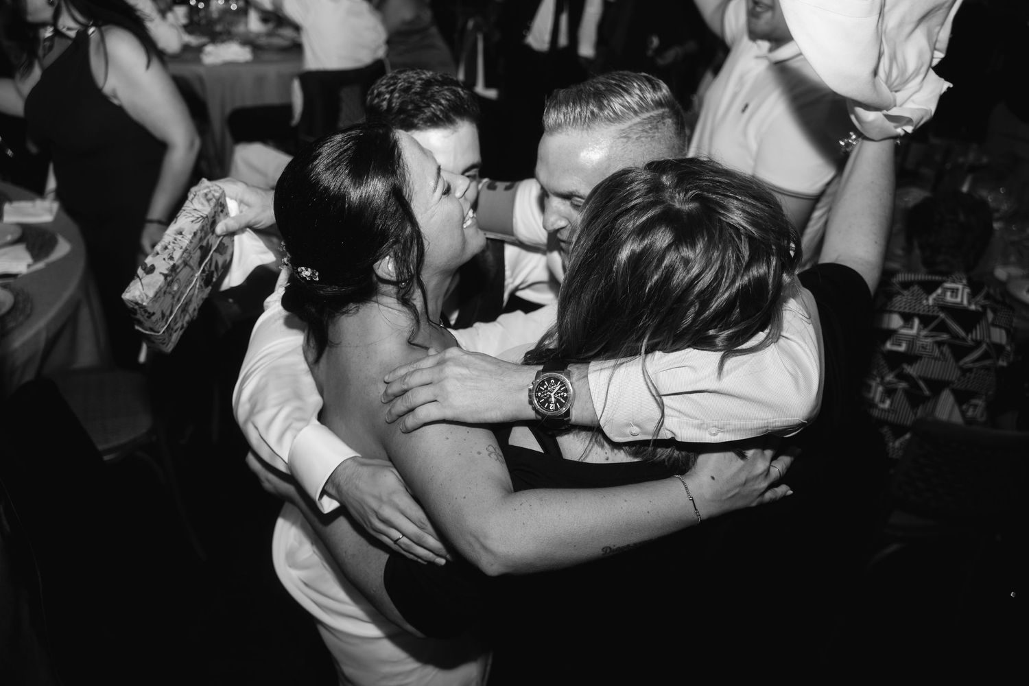 A black and white photo captures an energetic dance floor moment at a wedding celebration.