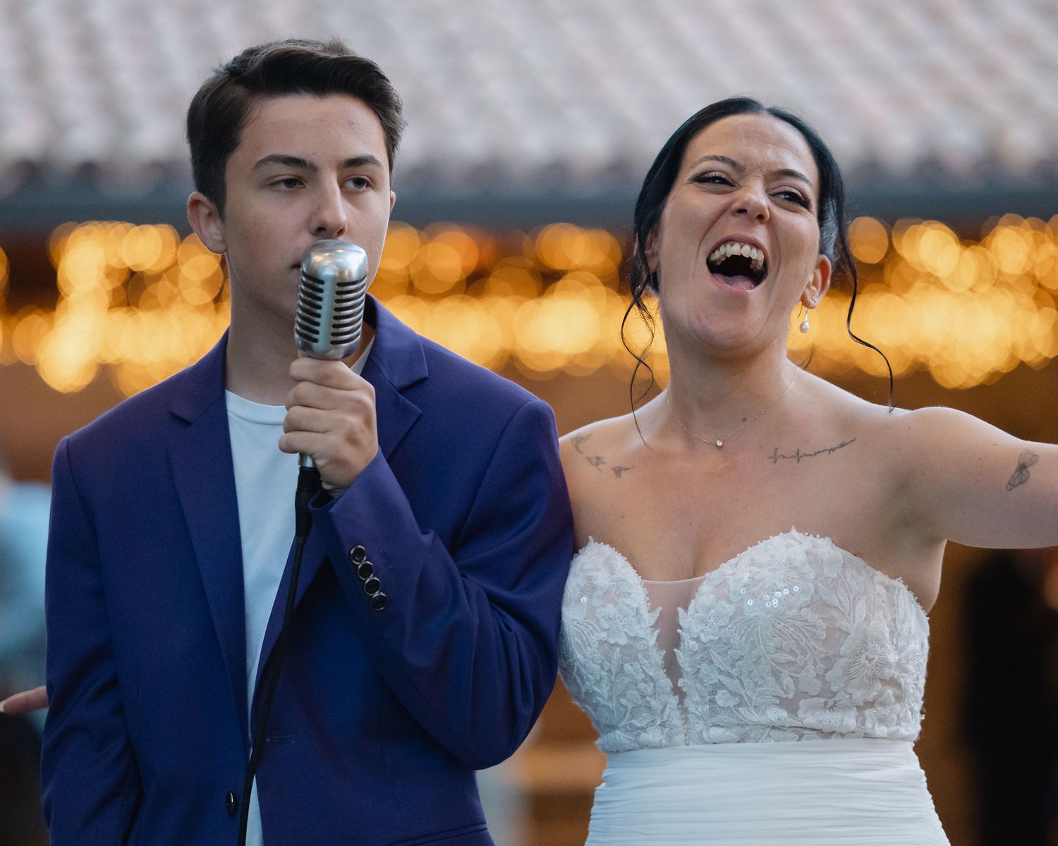 Newlyweds share a joyful moment dancing together at their wedding reception with warm bokeh lights in background.