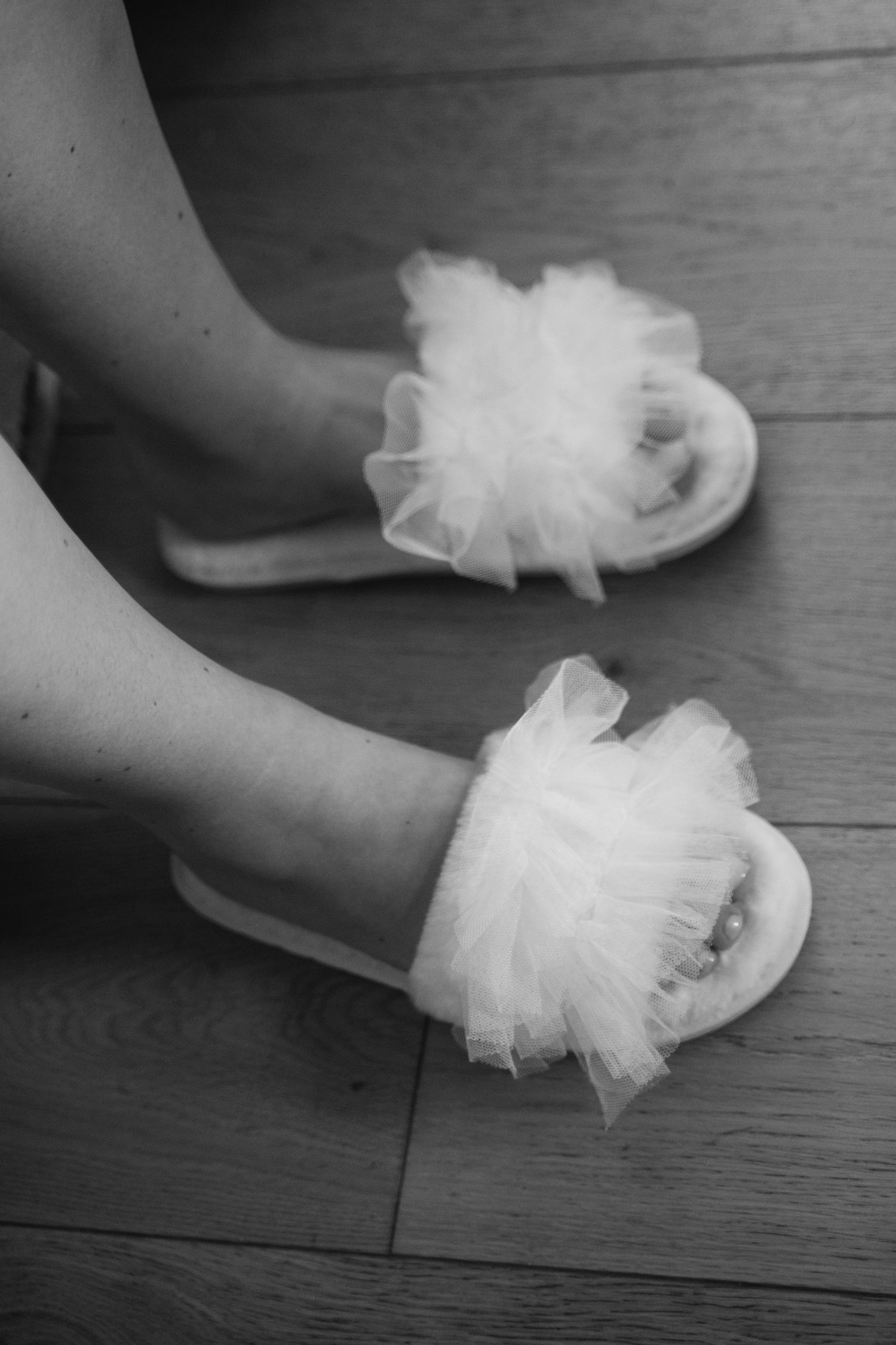 A pair of white tulle ballet slippers with satin ribbons rests on a dark wooden floor.