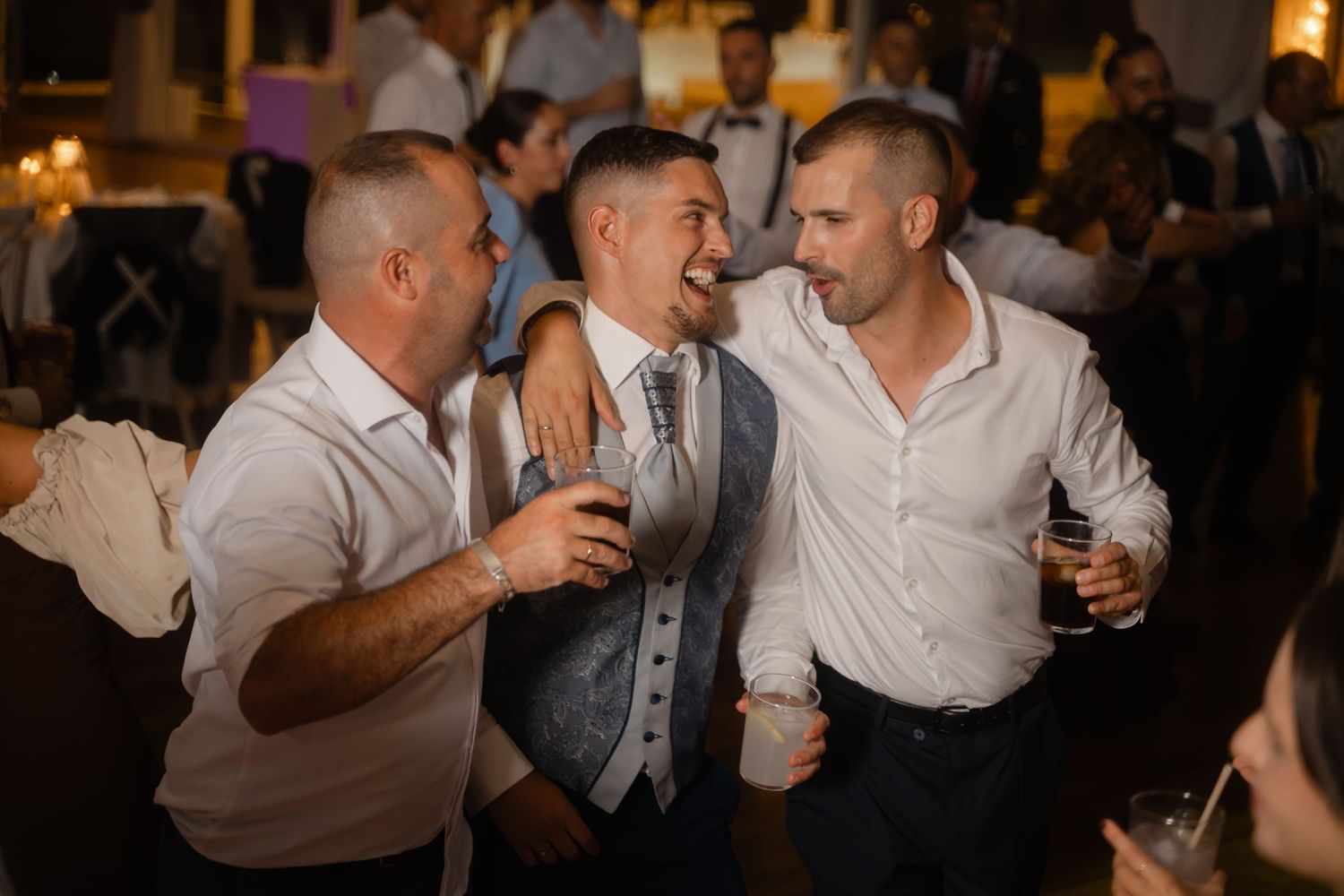 Three guests in formal attire share laughs and drinks during a lively reception celebration.