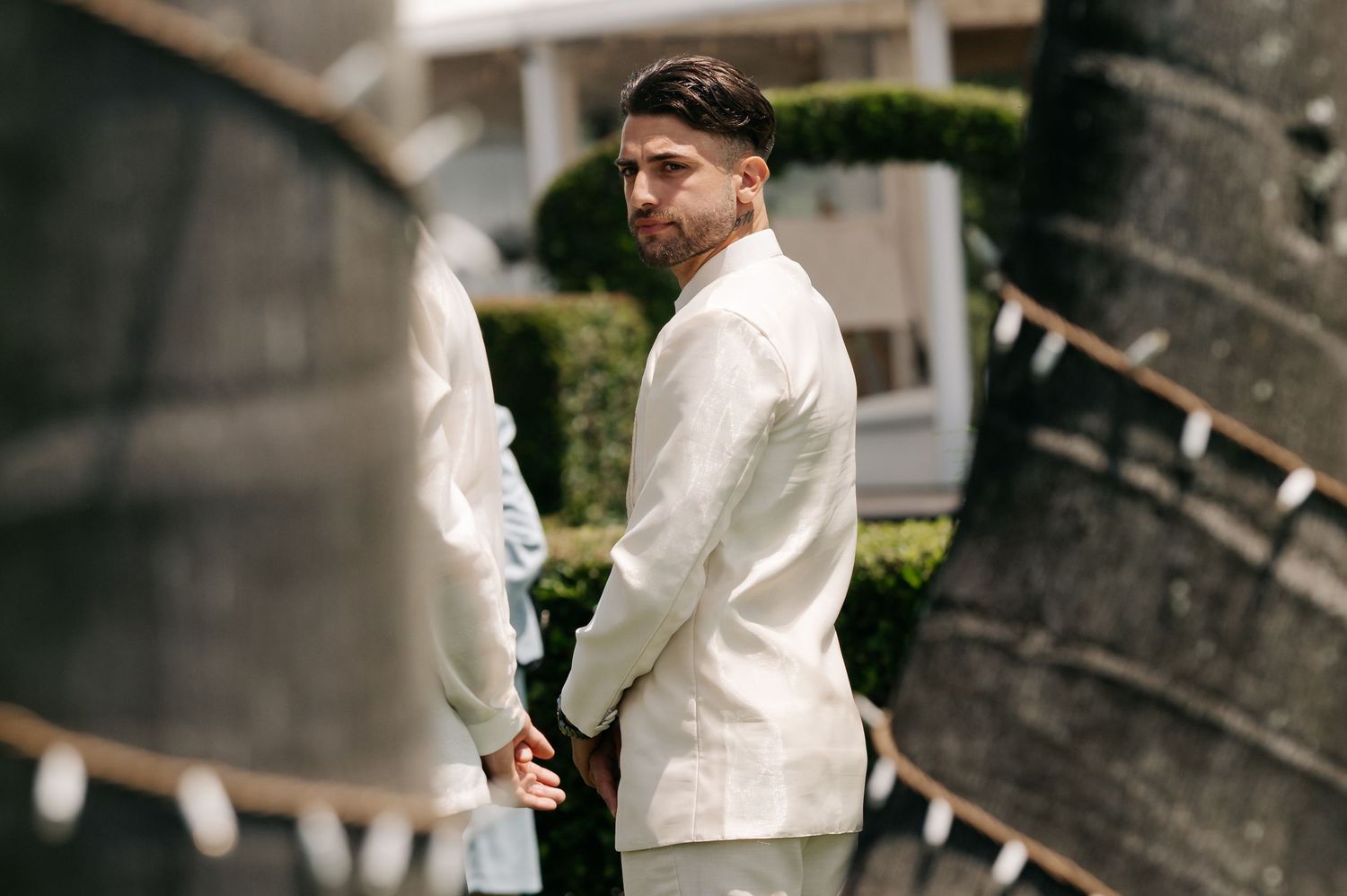 A couple in traditional wedding attire stand together in a garden setting during their outdoor ceremony.