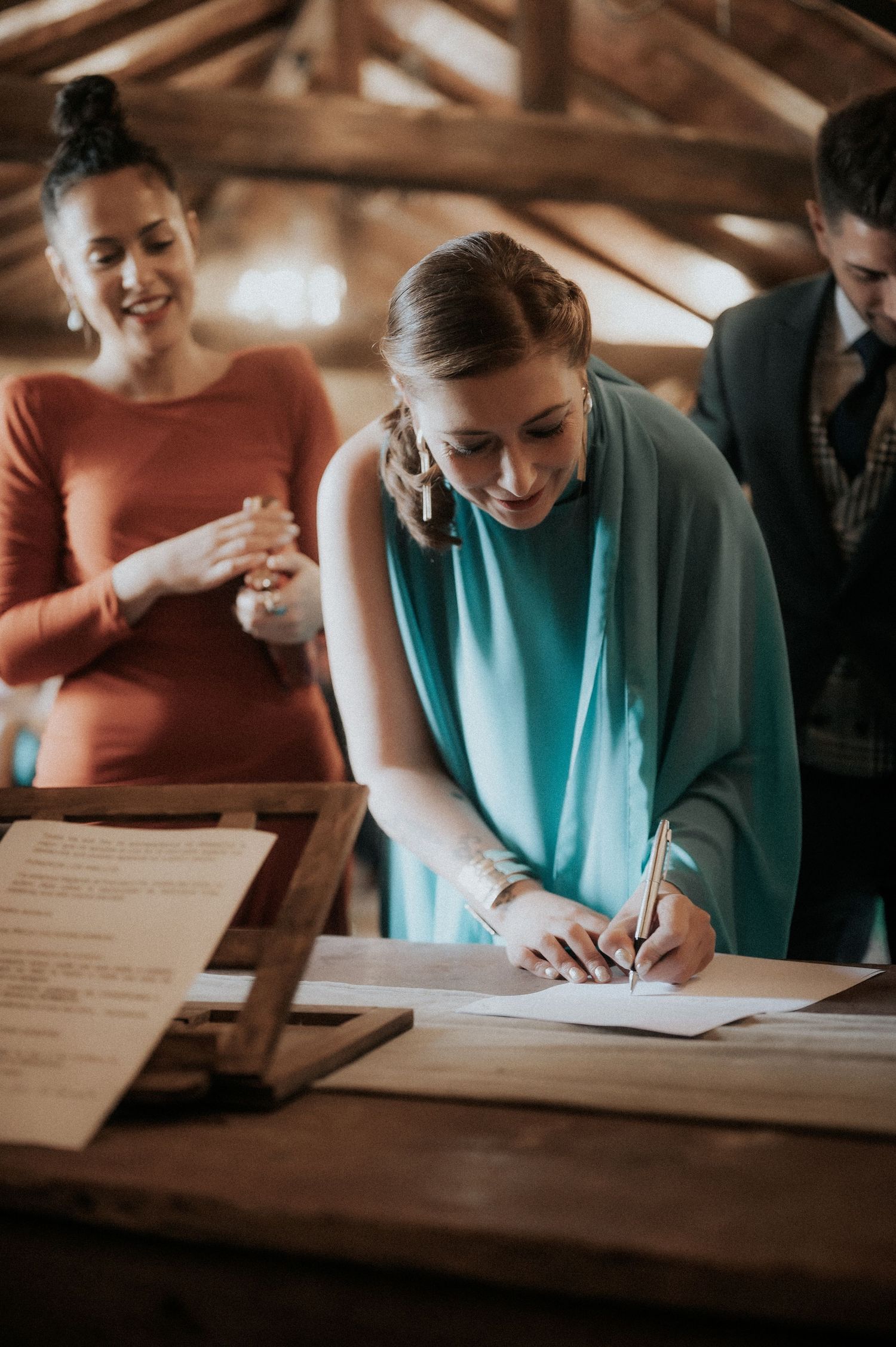 Wedding guests in colorful attire signing the marriage register or guestbook at a wooden table.