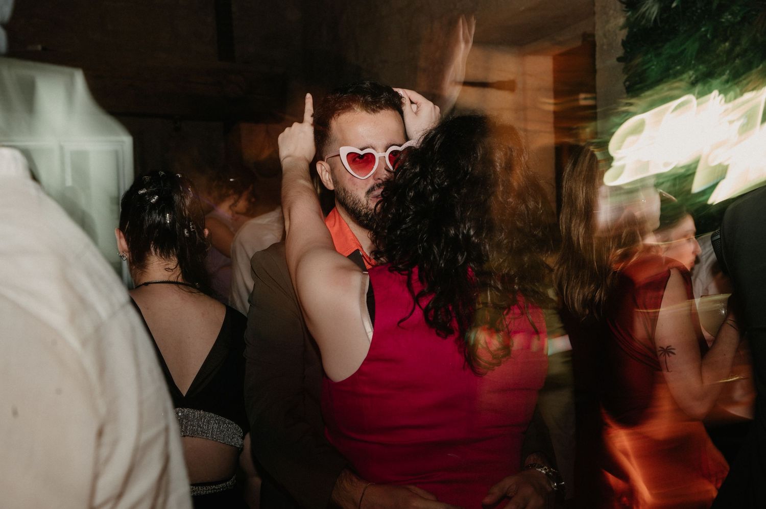 People dance and socialize at a dimly lit party venue with colorful lighting effects.