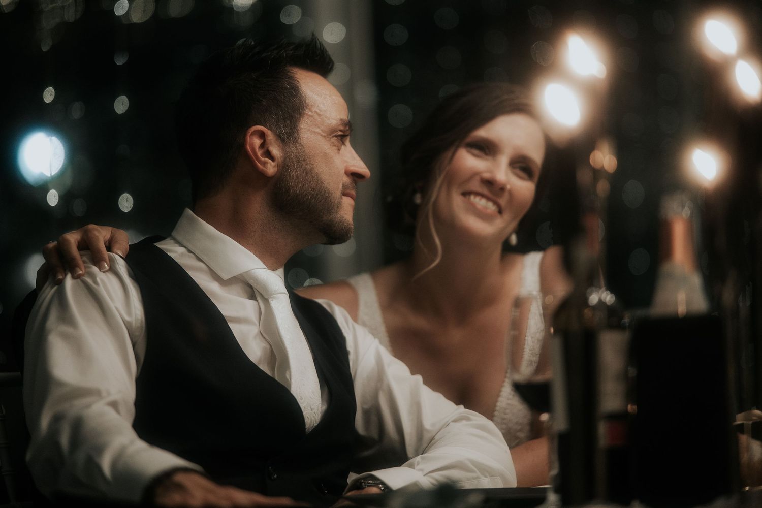A romantic couple shares tender moments in dim lighting with bokeh effects and string lights in the background.