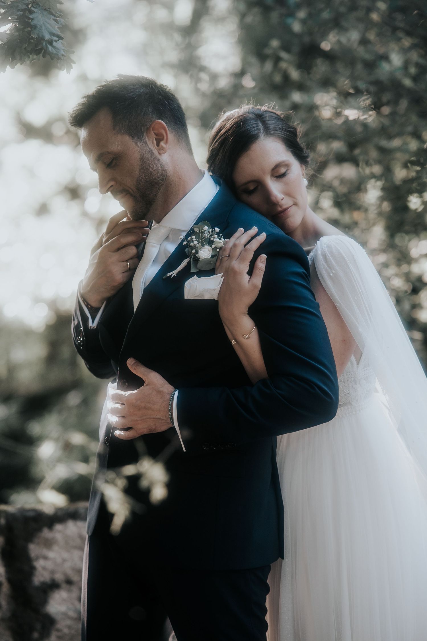 Emotional wedding embrace photographed in moody natural lighting with flowing veil details.